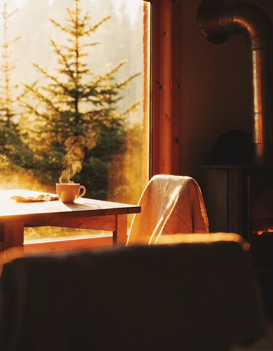 Intérieur chaleureux d'une cabane au coucher du soleil, forêt de sapins par la fenêtre